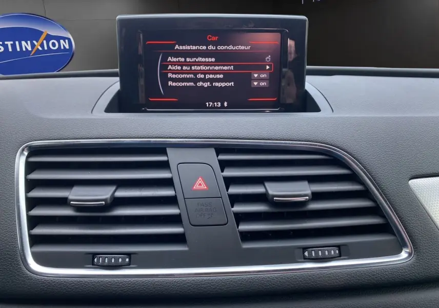 Vue intérieure du tableau de bord de l'Audi Q3 2014, écran central affichant l'aide au stationnement et les aérateurs noirs.