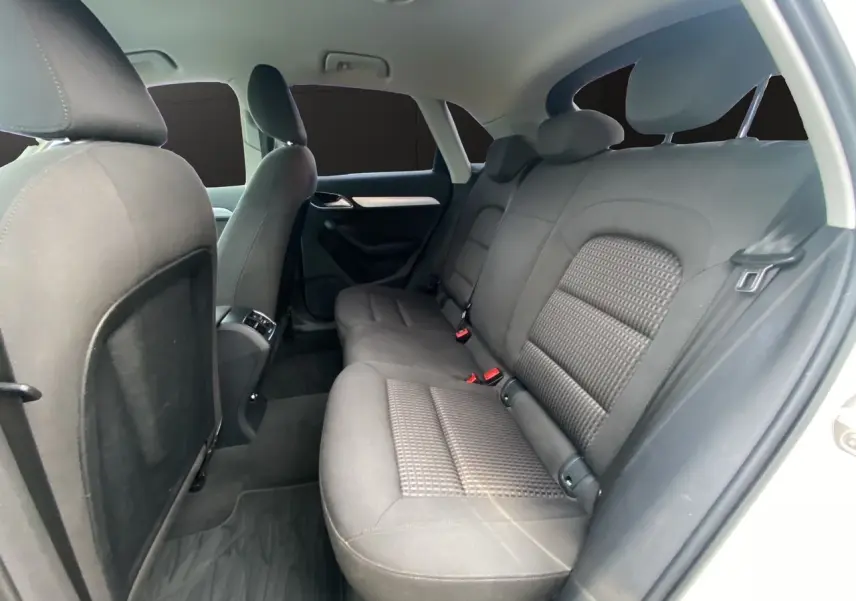 Vue intérieure montrant les sièges arrière en tissu noir de l'Audi Q3 blanc, version 2014, avec portes ouvertes côté droit.