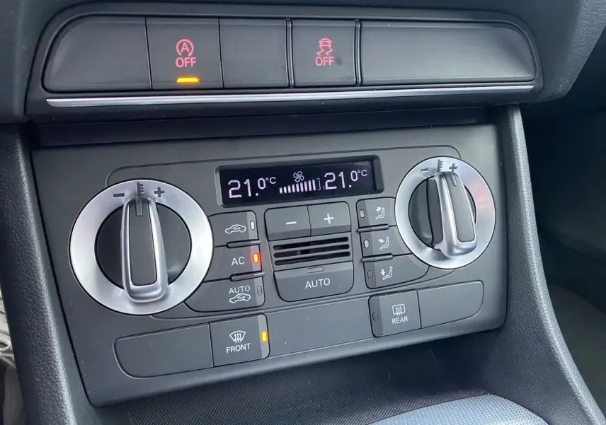Gros plan sur la console de climatisation automatique de l'Audi Q3 blanche, avec affichage digital et commandes rotatives.