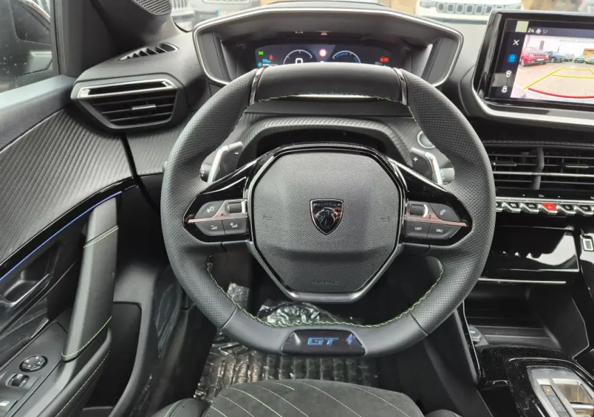 Vue intérieure centrée sur le volant GT de la Peugeot 208 gris, avec cockpit numérique et écran tactile visible.