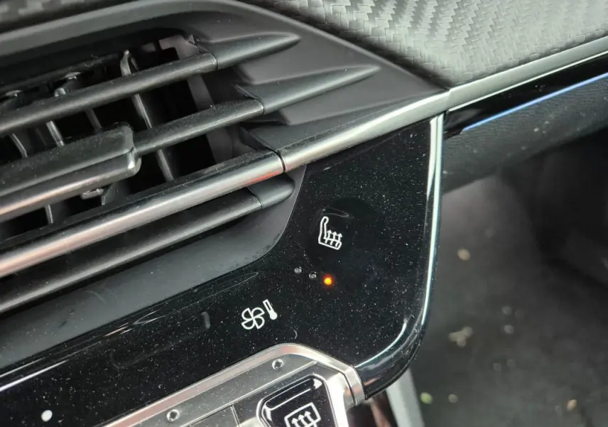 Détail du tableau de bord noir brillant de la Peugeot 208 gris, montrant le bouton de siège chauffant activé.