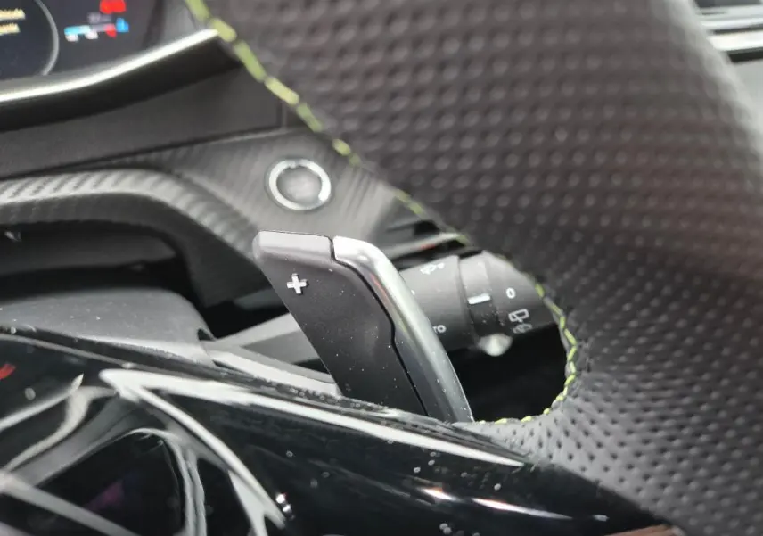 Gros plan sur la palette de changement de vitesse droite du volant perforé d’une Peugeot 208 Hybrid 110 e-DCS6 GT gris.