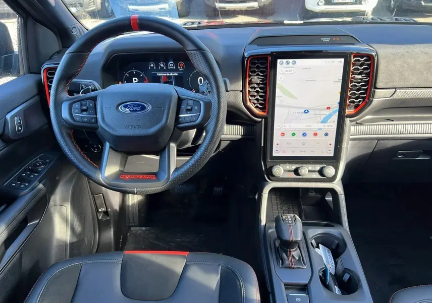 Vue intérieure avant du Ford Ranger Raptor noir, volant cuir avec surpiqûres rouges et grand écran tactile vertical central.