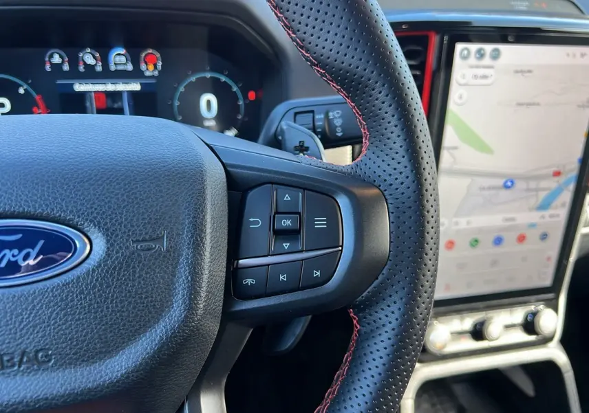 Gros plan sur le volant cuir perforé avec surpiqûres rouges du Ford Ranger Raptor 2025, écran tactile de navigation visible.