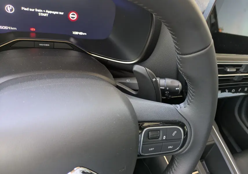 Gros plan sur le volant en cuir noir du Citroën C5 Aircross Hybride 2025 avec commandes intégrées et tableau de bord numérique.