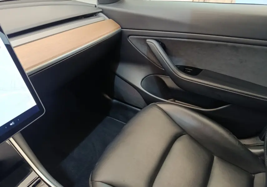 Vue intérieure côté passager d'une Tesla Model 3 2020 avec tableau de bord bois clair et siège cuir noir.
