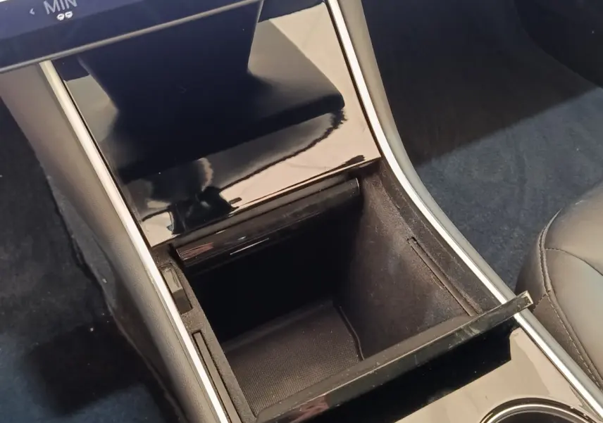 Vue rapprochée de la console centrale noire brillante avec rangement ouvert et accoudoir cuir dans une Tesla Model 3 bleu.
