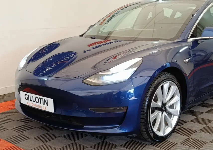 Vue 3/4 avant droite d'une Tesla Model 3 Long Range bleu électrique avec phares LED et jantes argentées.