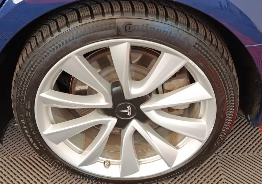 Gros plan sur la jante argentée et le pneu Continental d'une Tesla Model 3 bleu, côté gauche avant.