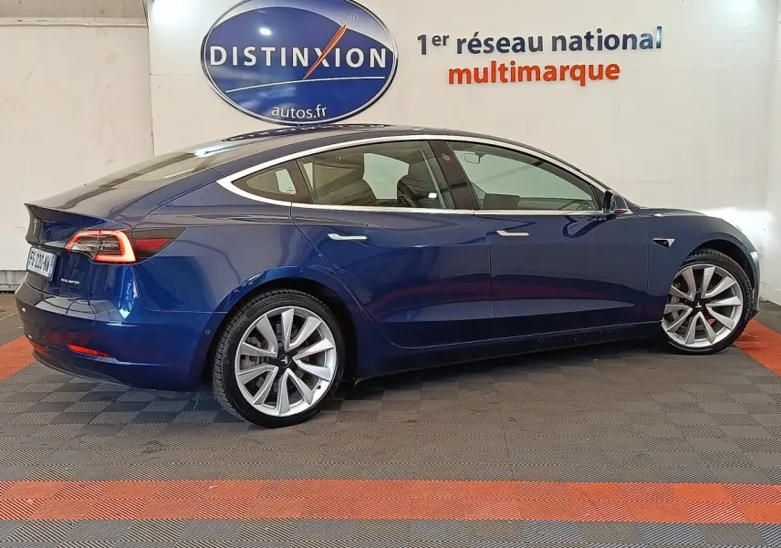 Profil droit d'une Tesla Model 3 Long Range bleu électrique, avec jantes alliage et feux arrière LED distinctifs.
