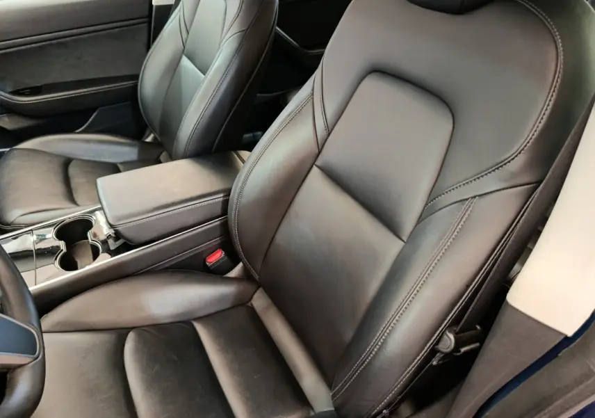 Vue intérieure rapprochée des sièges avant en cuir noir d’une Tesla Model 3 Long Range bleu, avec console centrale visible.