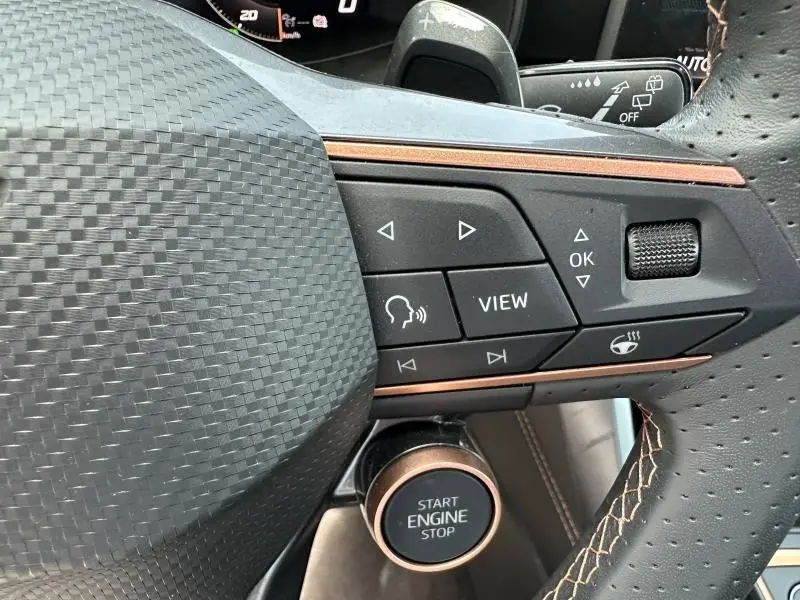 Gros plan sur les commandes multifonctions et bouton start/stop du volant cuir perforé du CUPRA Formentor bleu 2025.