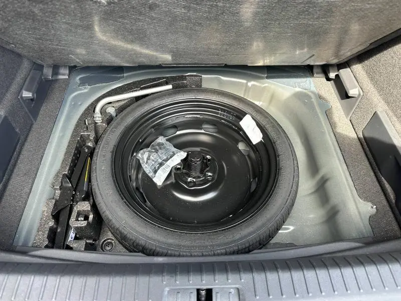 Vue plongeante sur la roue de secours noire dans le coffre du CUPRA Formentor bleu, avec outils de changement visibles.