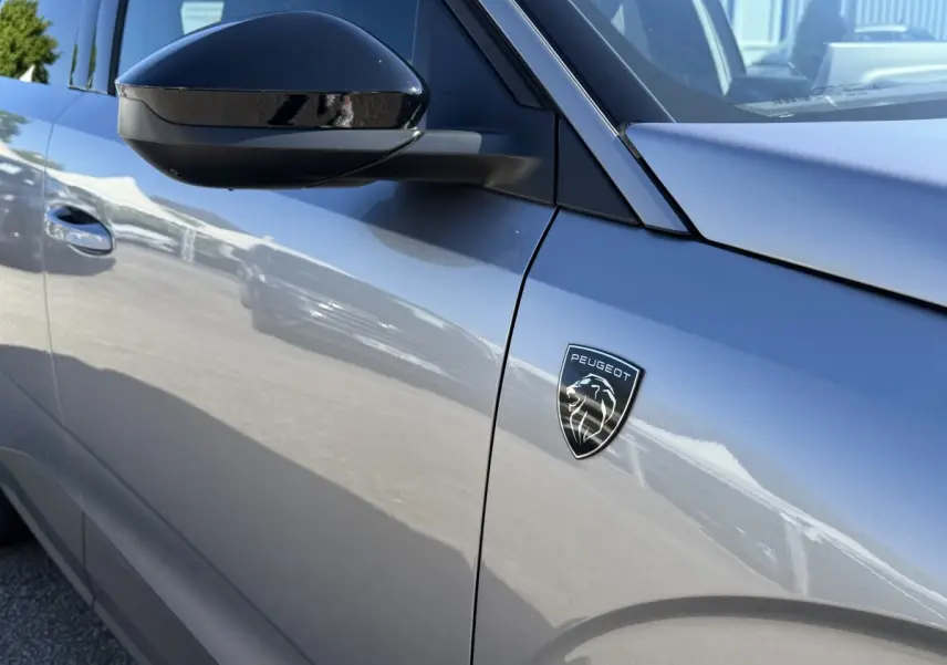 Gros plan sur le côté gauche gris clair du Peugeot 3008 2025 avec logo Peugeot et rétroviseur noir brillant.