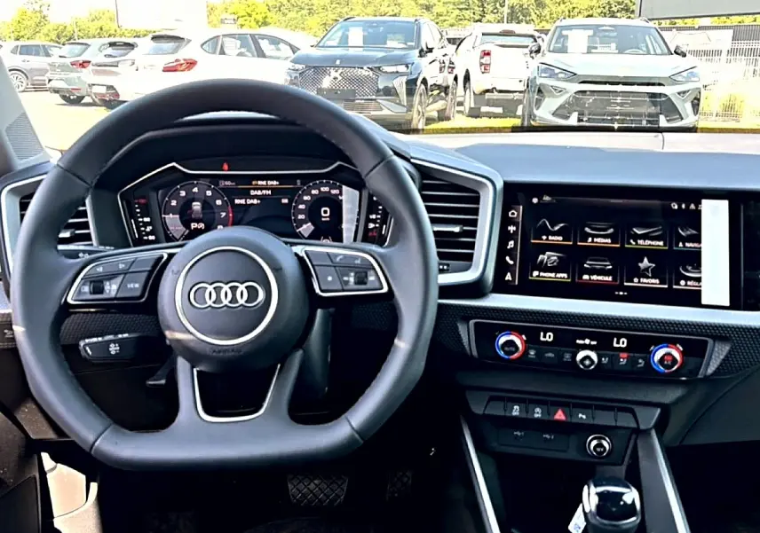 Vue intérieure centrée sur le volant multifonction et l'écran tactile du tableau de bord de l'Audi A1 Sportback noir.