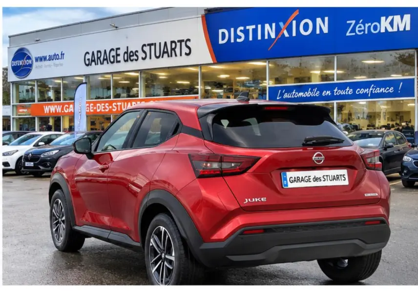 Vue 3/4 arrière droite du Nissan Juke rouge Fuji Sunset garé devant un garage avec jantes alliage 17 pouces.