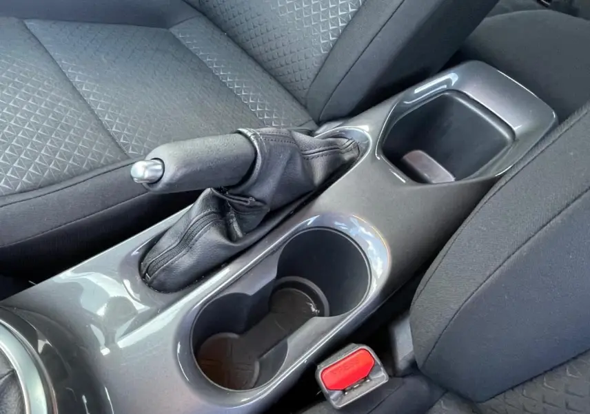 Gros plan sur la console centrale grise du Nissan Juke 2024, montrant frein à main manuel et porte-gobelets noirs.