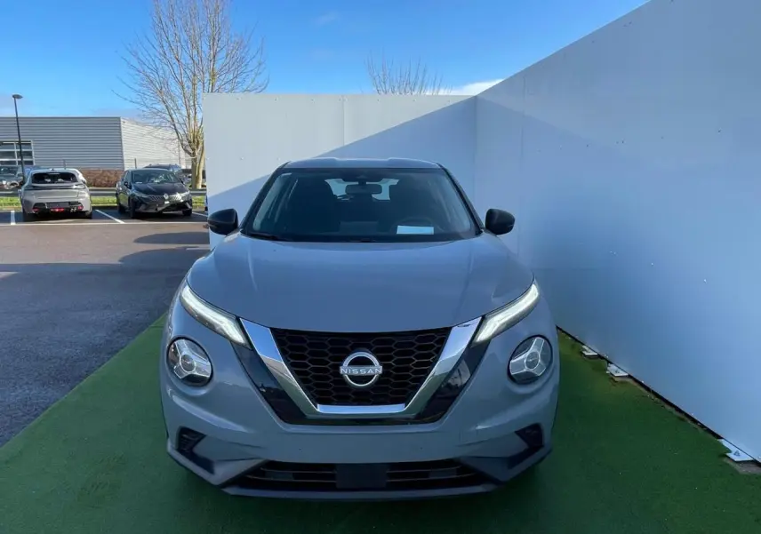 Nissan Juke II gris ceramic vu de face, soulignant sa calandre en V chromée et ses phares LED ronds.