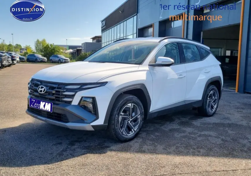 Hyundai Tucson blanc atlas en 3/4 avant droit, avec calandre grise et jantes alliage 17 pouces distinctives.