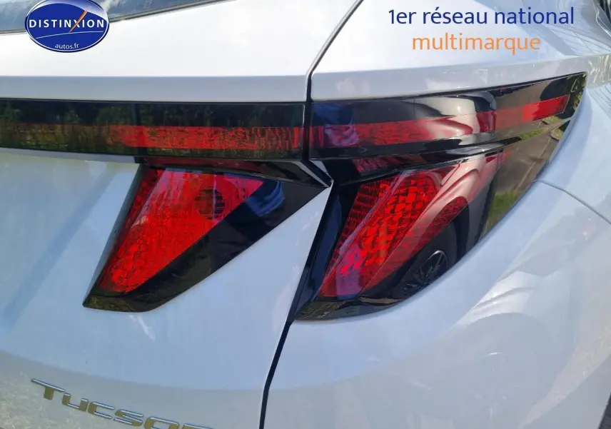 Gros plan sur le feu arrière droit rouge du Hyundai Tucson blanc atlas 2025 avec calandre grise et jante alliage visible en reflet.