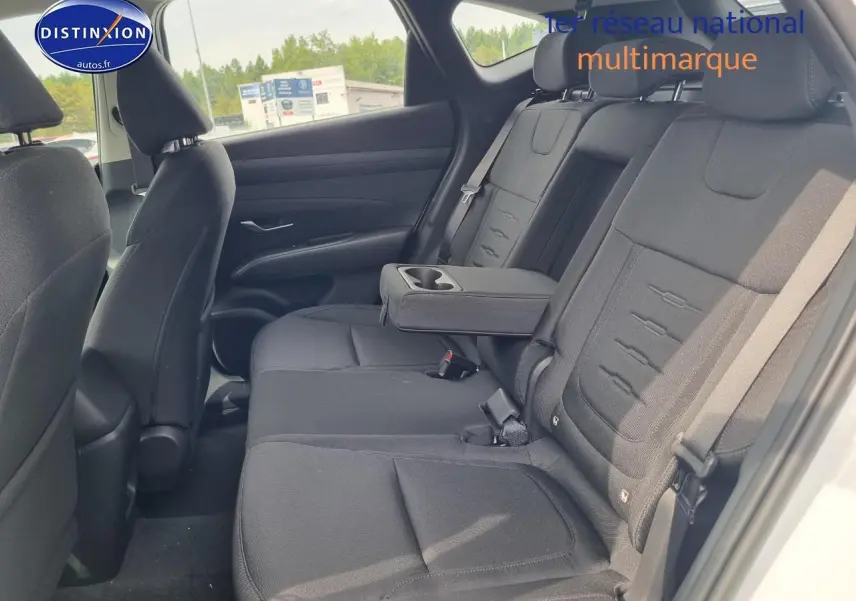 Vue intérieure côté droit des sièges arrière noirs avec accoudoir central déployé du Hyundai Tucson blanc atlas 2025.