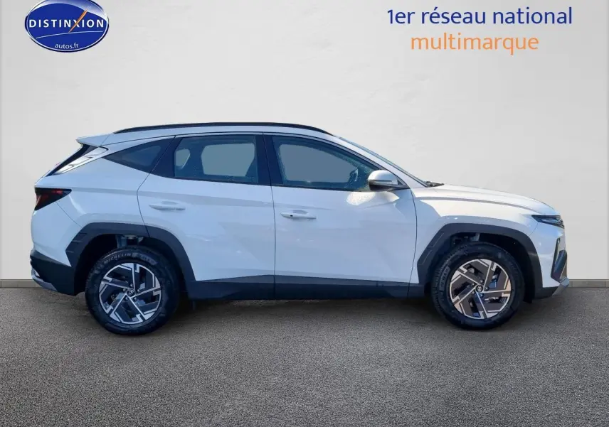 Profil droit d'un Hyundai Tucson blanc atlas 2025 avec jantes alliage et barres de toit noires visibles.