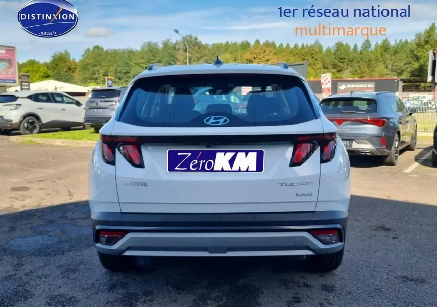 Vue arrière d'un Hyundai Tucson blanc atlas hybride avec feux arrière sombres et barres de toit visibles.