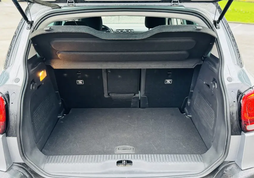 Coffre ouvert vu de l'arrière d'un Citroën C3 Aircross gris Artense avec banquette arrière et cache-bagages visibles.