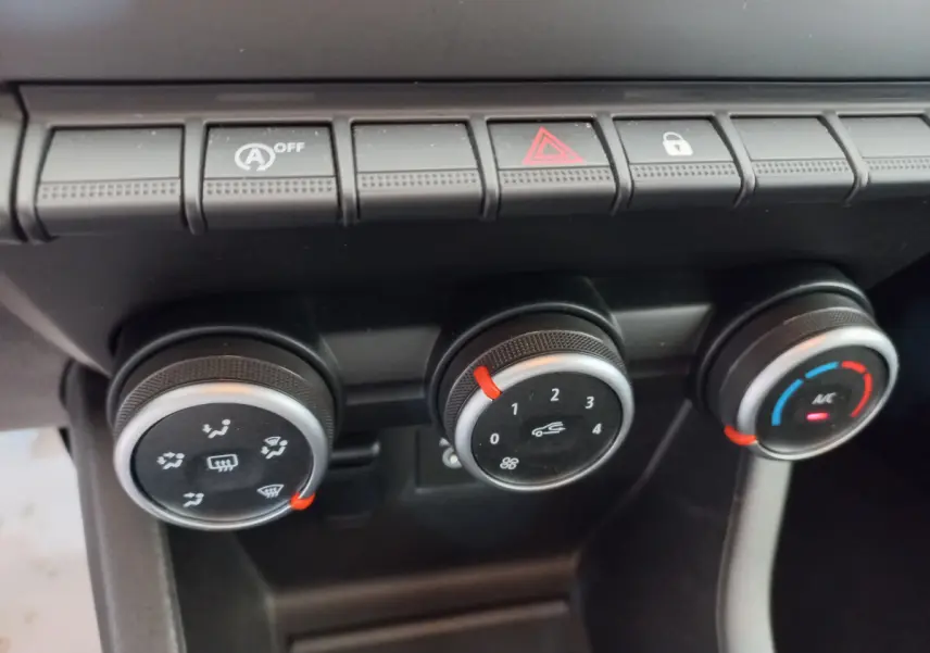 Gros plan sur les commandes de climatisation et boutons de fonction du tableau de bord noir de la Renault Clio Business blanche.