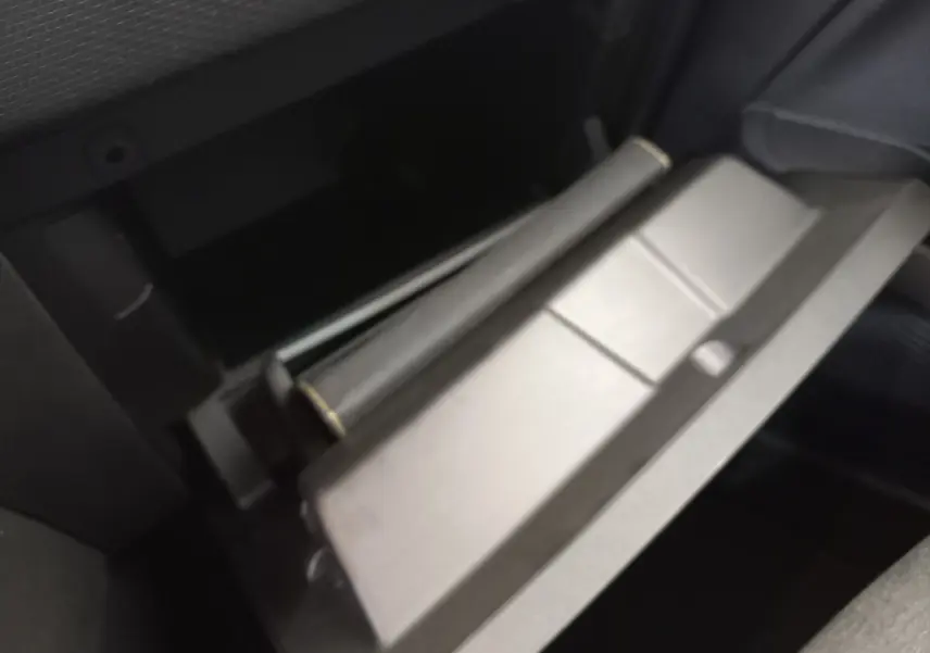 Gros plan sur la boîte à gants ouverte de la Renault Clio Business blanche, montrant l'intérieur sombre et le rangement.