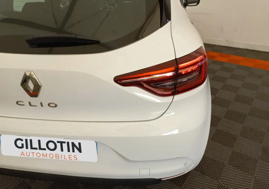 Vue arrière droite d'une Renault Clio Business blanche avec feux arrière LED et logo visible sur un sol à damiers.