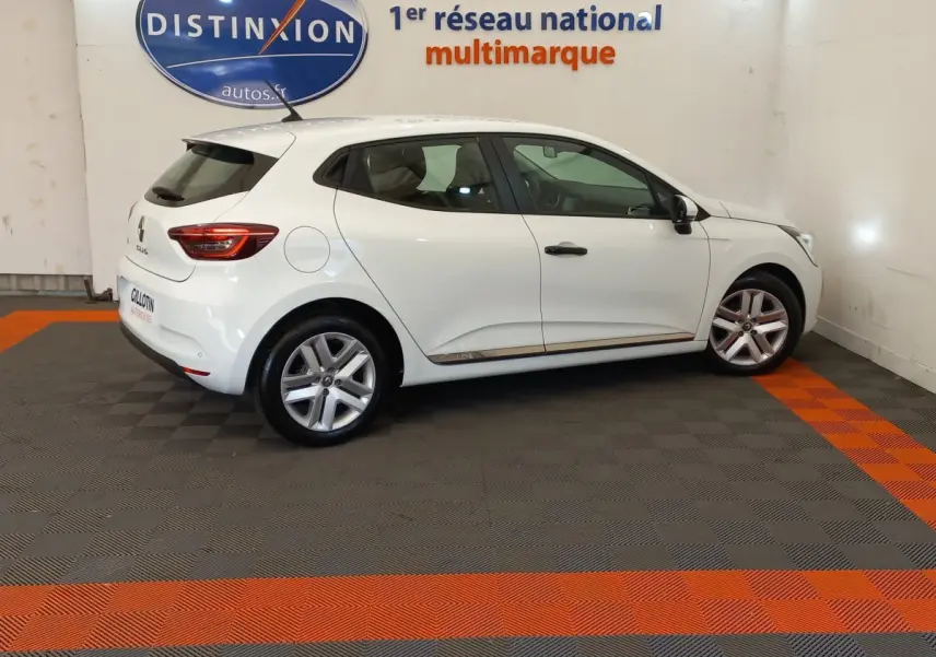 Profil droit d'une Renault Clio Business blanche 2021, avec jantes alliage et feux arrière LED visibles en intérieur showroom.
