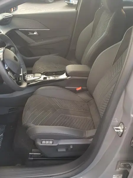 Vue intérieure côté conducteur de la Peugeot 208 Hybrid 110 e-DCS6 GT 2025 gris, sièges en tissu avec réglages électriques et volant réglable.