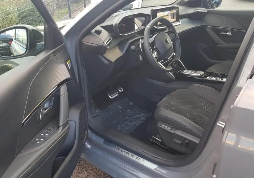 Vue intérieure côté conducteur de la Peugeot 208 Hybrid gris 2025, avec volant GT, écran tactile et sièges en alcantara.