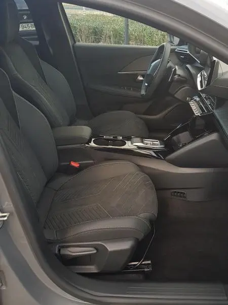 Vue intérieure côté conducteur de la Peugeot 208 Hybrid gris 2025, avec sièges en tissu et cockpit numérique visible.
