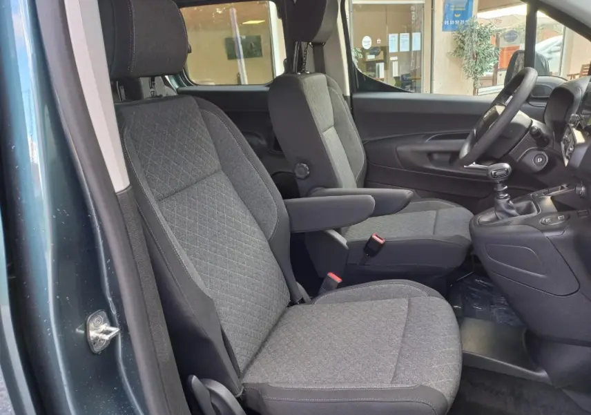 Vue intérieure côté conducteur de l’Opel Combo Life M 2025 bleu, montrant les sièges avant gris et la boîte manuelle.