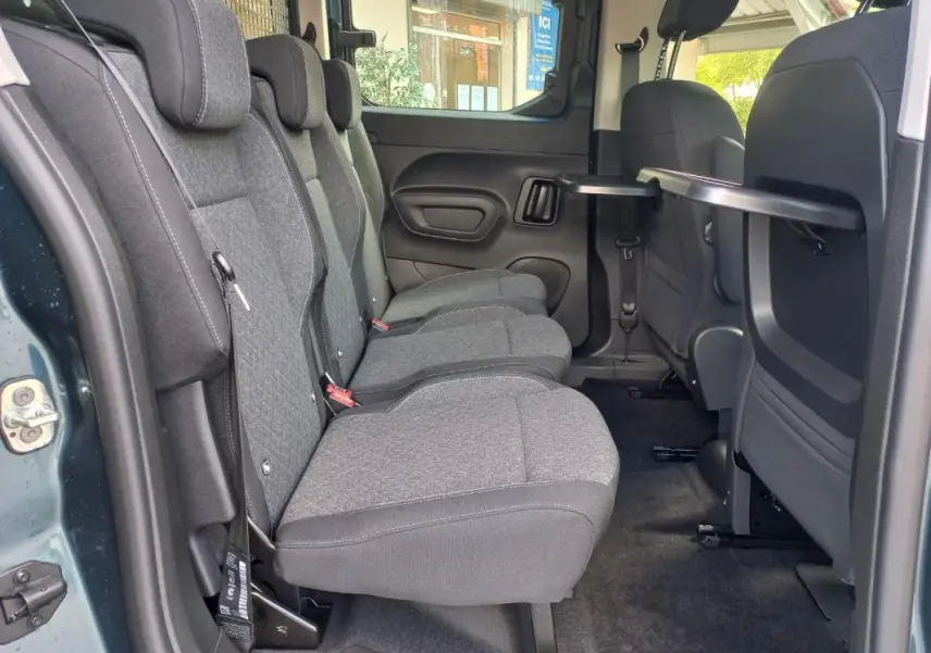 Vue intérieure côté gauche des sièges arrière gris du Opel Combo Life M 2025 avec tablette rabattable sur dossier avant.