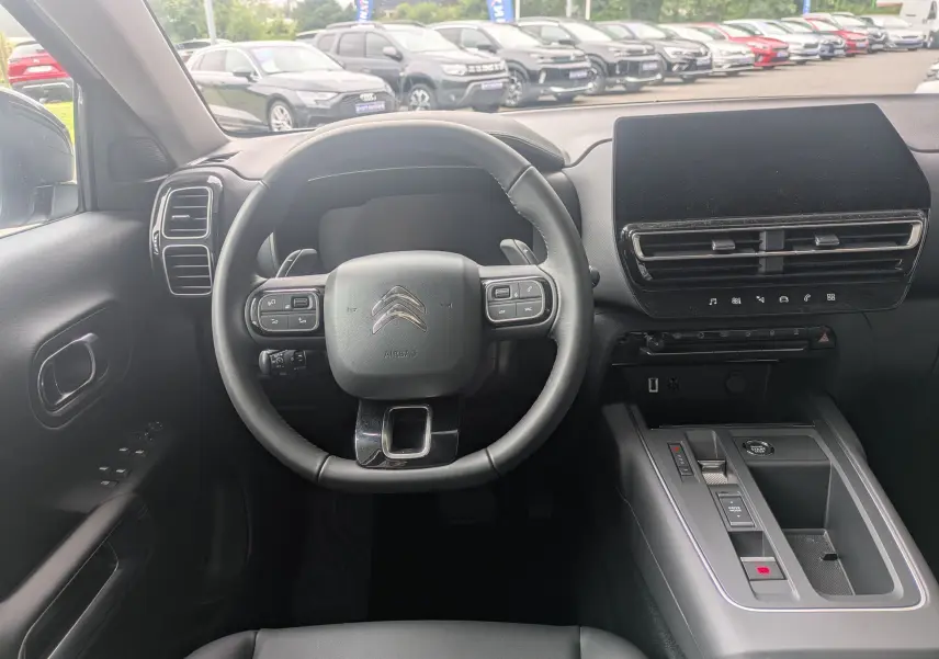 Vue intérieure centrée sur le volant et la console centrale du Citroën C5 Aircross hybride 2025, ambiance noire moderne.