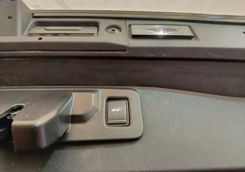 Bouton d'ouverture électrique du coffre sur la partie intérieure de la porte arrière du Renault Symbioz noir.