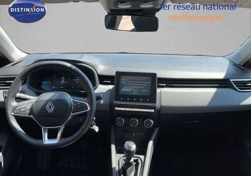 Vue intérieure avant du tableau de bord et volant de la Renault Clio rouge flamme, avec écran tactile et boîte manuelle.