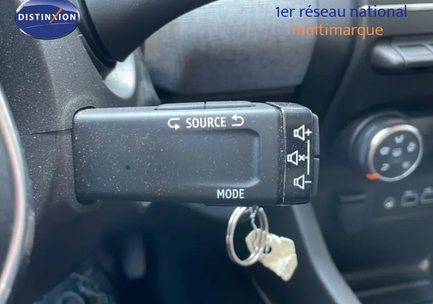 Gros plan sur la commande au volant gauche de la Renault Clio rouge flamme, avec bouton source et mode visible.