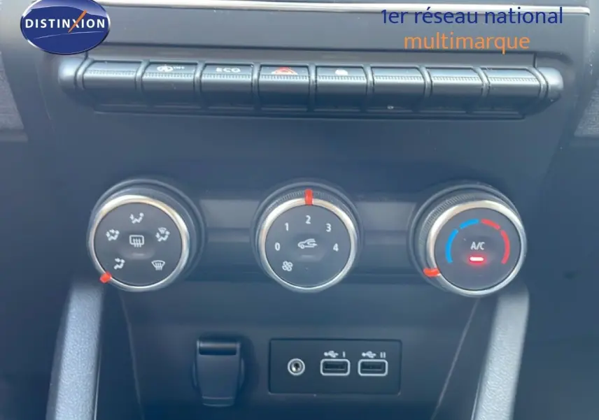 Gros plan sur les commandes de climatisation et les ports USB du tableau de bord d’une Renault Clio rouge flamme 2025.