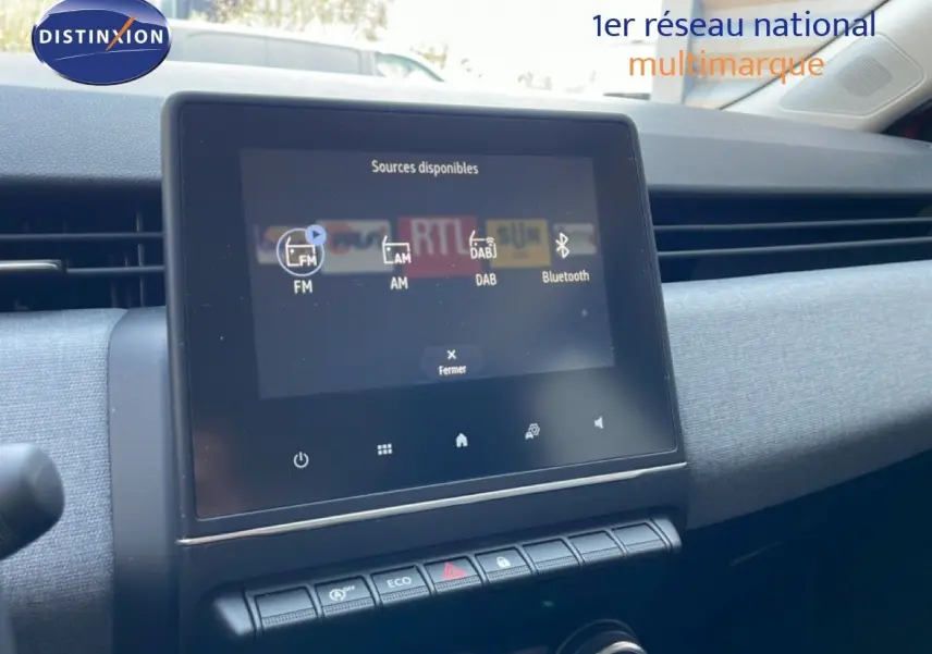 Écran tactile central affichant les sources audio dans l’habitacle d’une Renault Clio rouge flamme métal, vue de face.