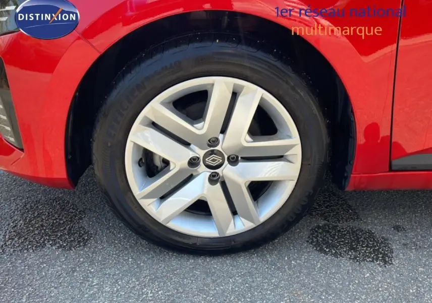 Gros plan sur la roue avant gauche de la Renault Clio rouge flamme métal, mettant en valeur la jante alliage moderne.
