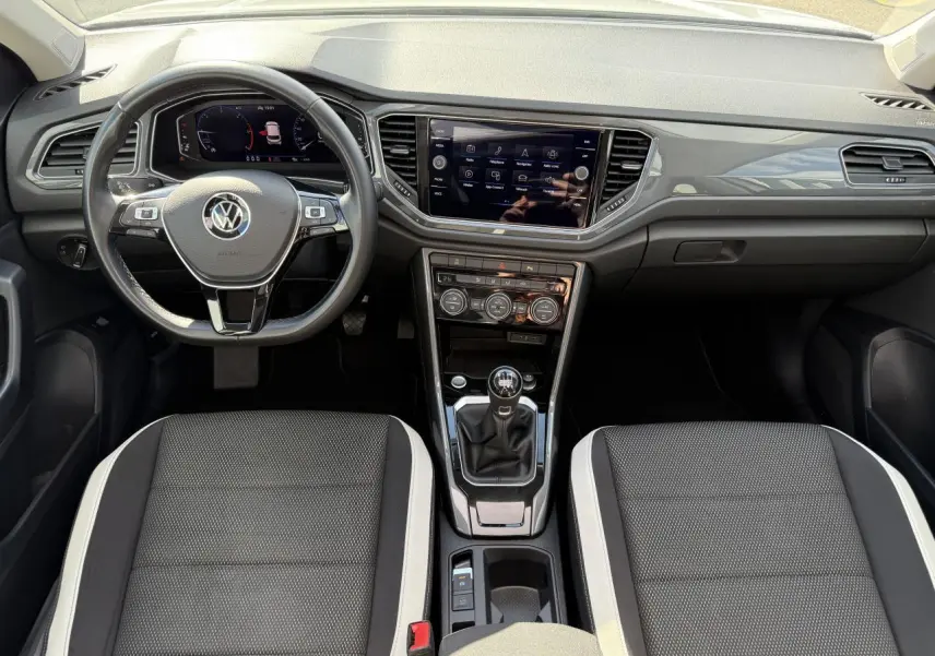 Vue intérieure avant du Volkswagen T-Roc blanc 2022, tableau de bord moderne avec écran tactile et volant multifonction cuir.