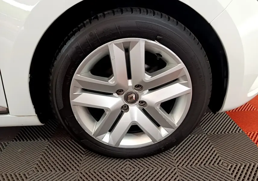 Gros plan sur la roue avant gauche d'une Renault Clio blanche, jante alliage au design moderne.