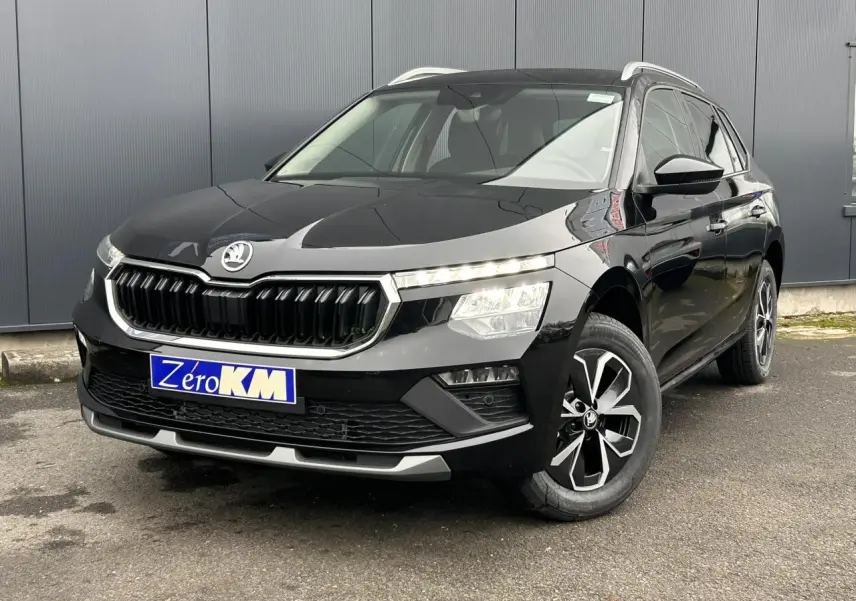 Vue 3/4 avant d'un Skoda Kamiq noir Magic avec jantes alliage et calandre chromée, stationné devant un mur gris.