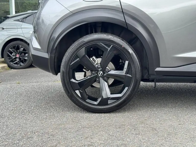 Gros plan sur la roue avant droite noire Kuro métallisée du Nissan Juke 2025 avec jante alu noire au design géométrique.
