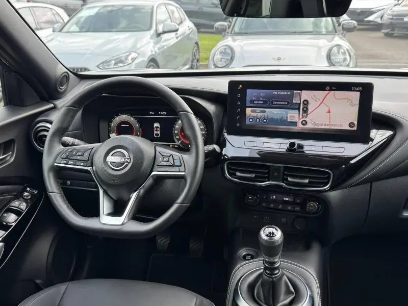 Vue intérieure avant du Nissan Juke 2025 noir, volant cuir multifonction et écran tactile central avec navigation.