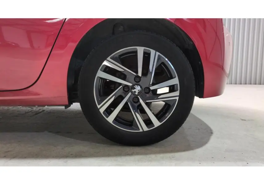 Gros plan sur la roue arrière droite d'une Peugeot 208 2024 rouge Elixir avec jante alliage bicolore.